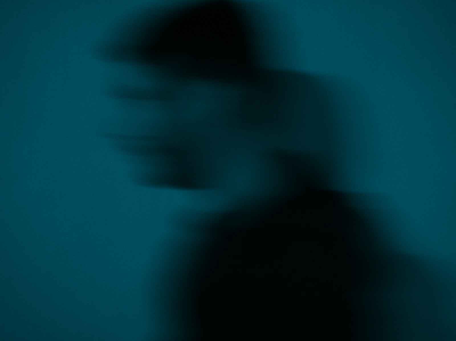 Blurred silhouette of a person against a teal background